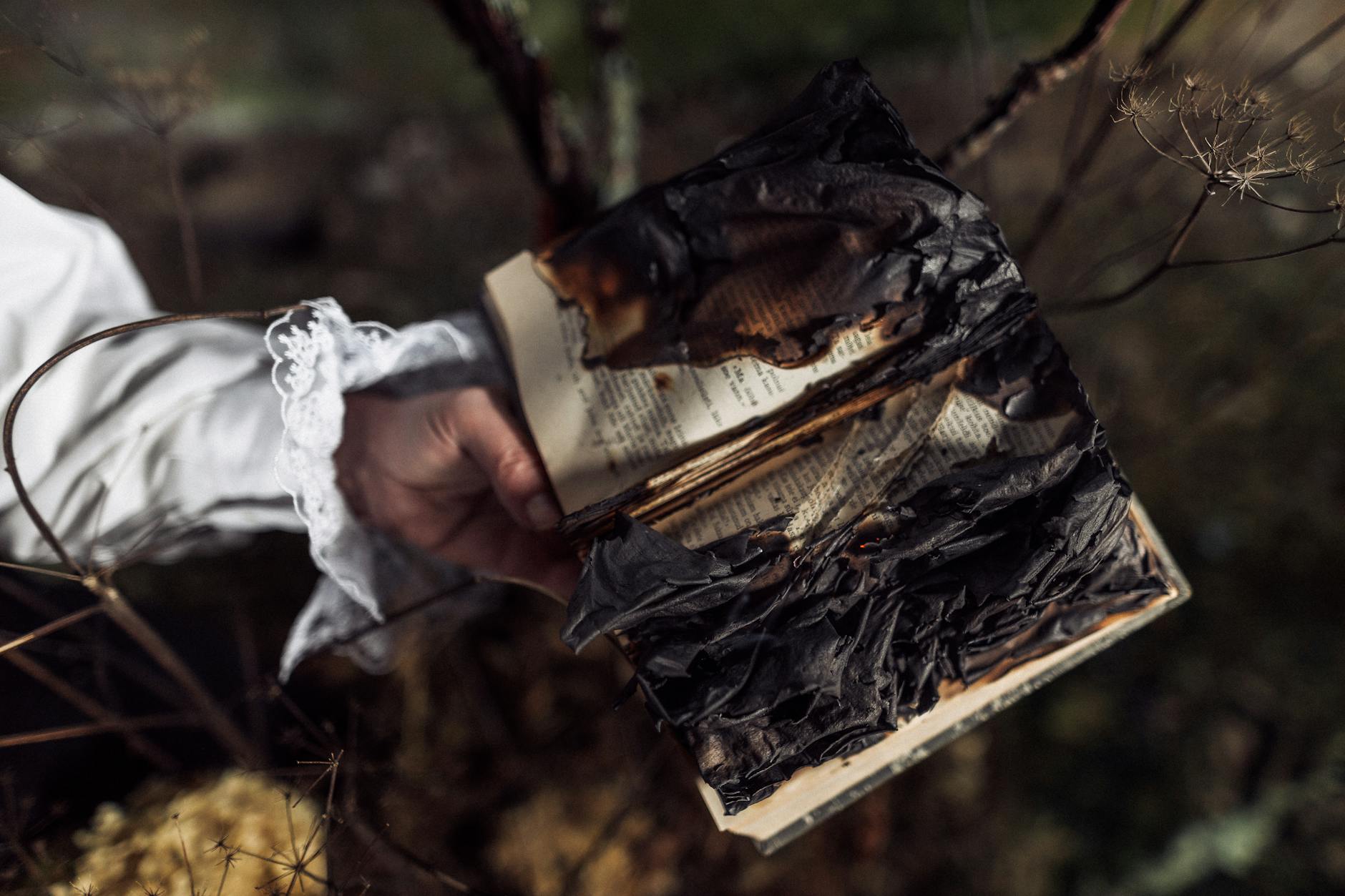 Dłoń trzyma nadpaloną książkę na tle zieleni, symboliczny motyw ognia