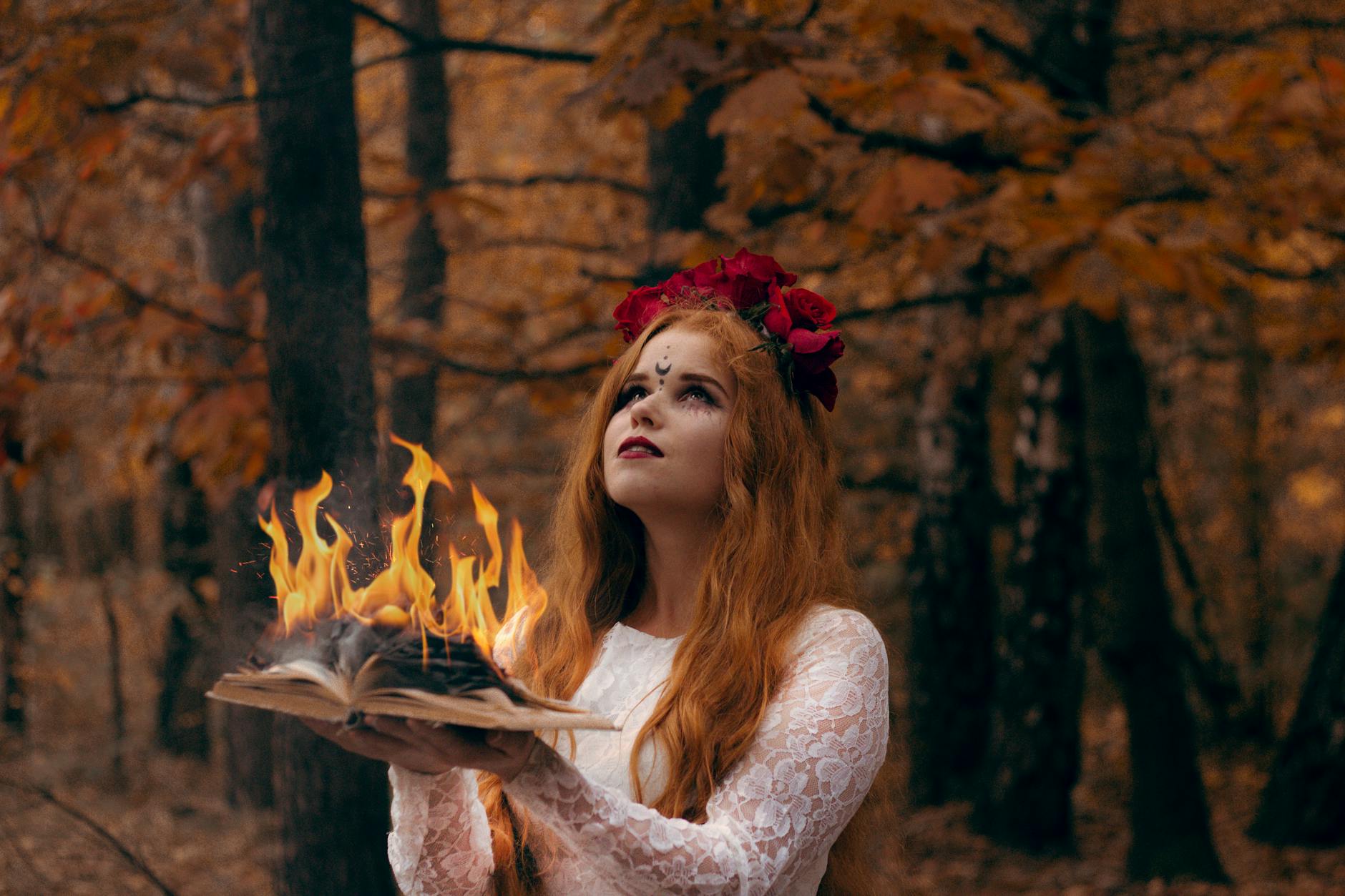 Motyw pożaru w literaturze: oczyszczenie, chaos i punkt zwrotny fabuły Kobieta o rudych włosach trzyma płonącą książkę w jesiennym lesie