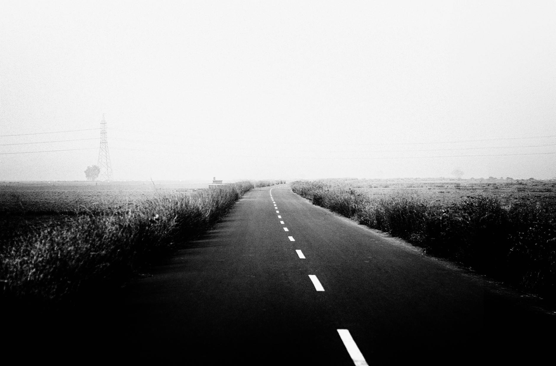 Czarno-biała wiejska droga we mgle, znikająca w oddali