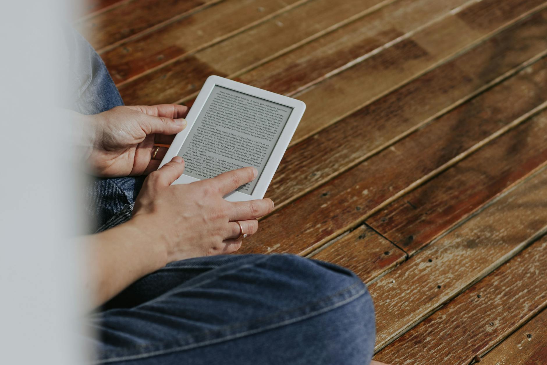 Czytnik ebooków trzymany w dłoniach na drewnianej podłodze