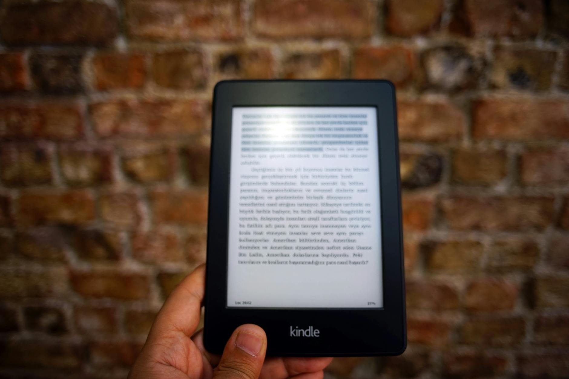 Kindle trzymany w dłoni na tle ceglanej ściany