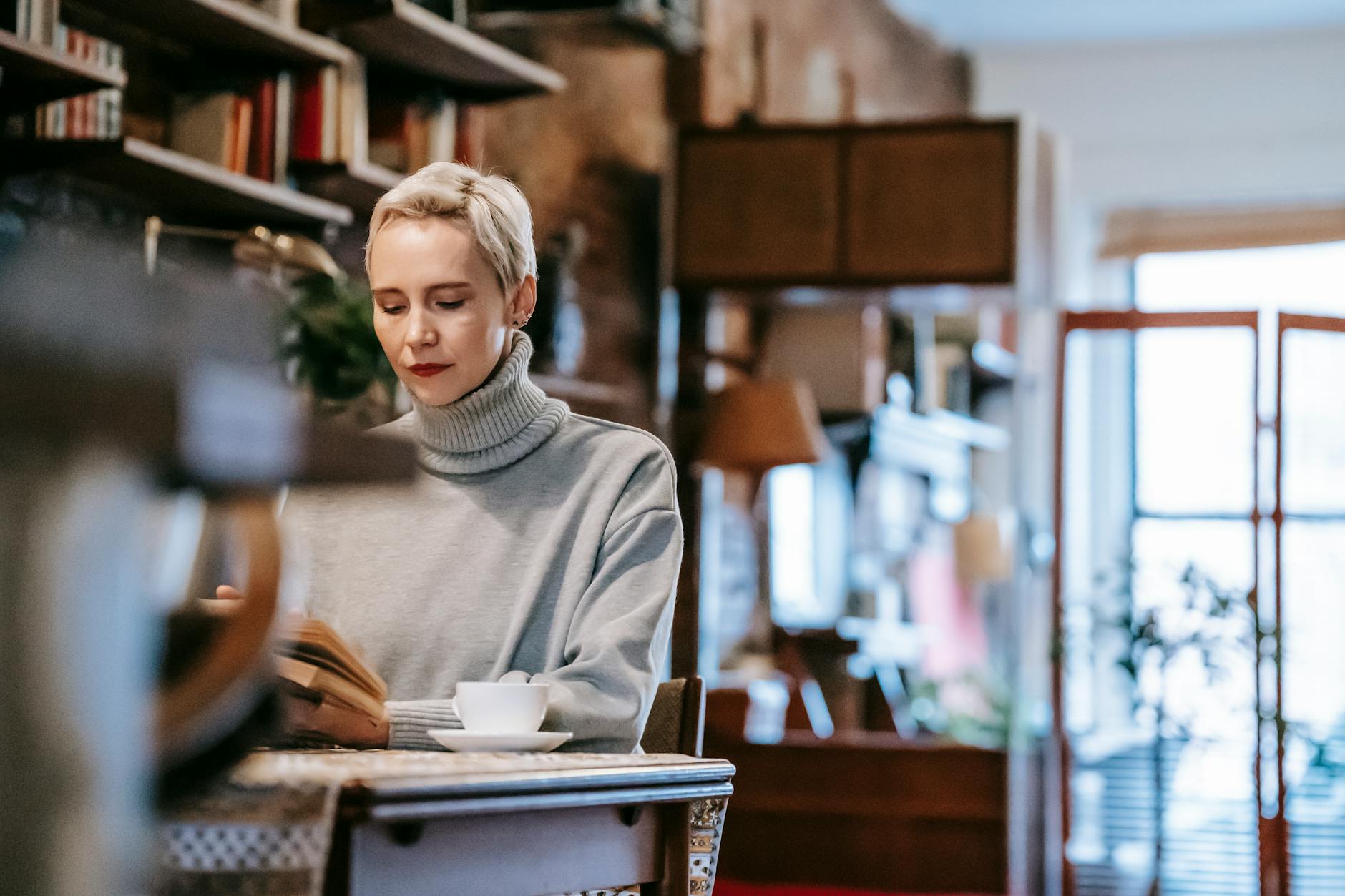 Kobieta przy stole w domu czyta książkę i pije kawę