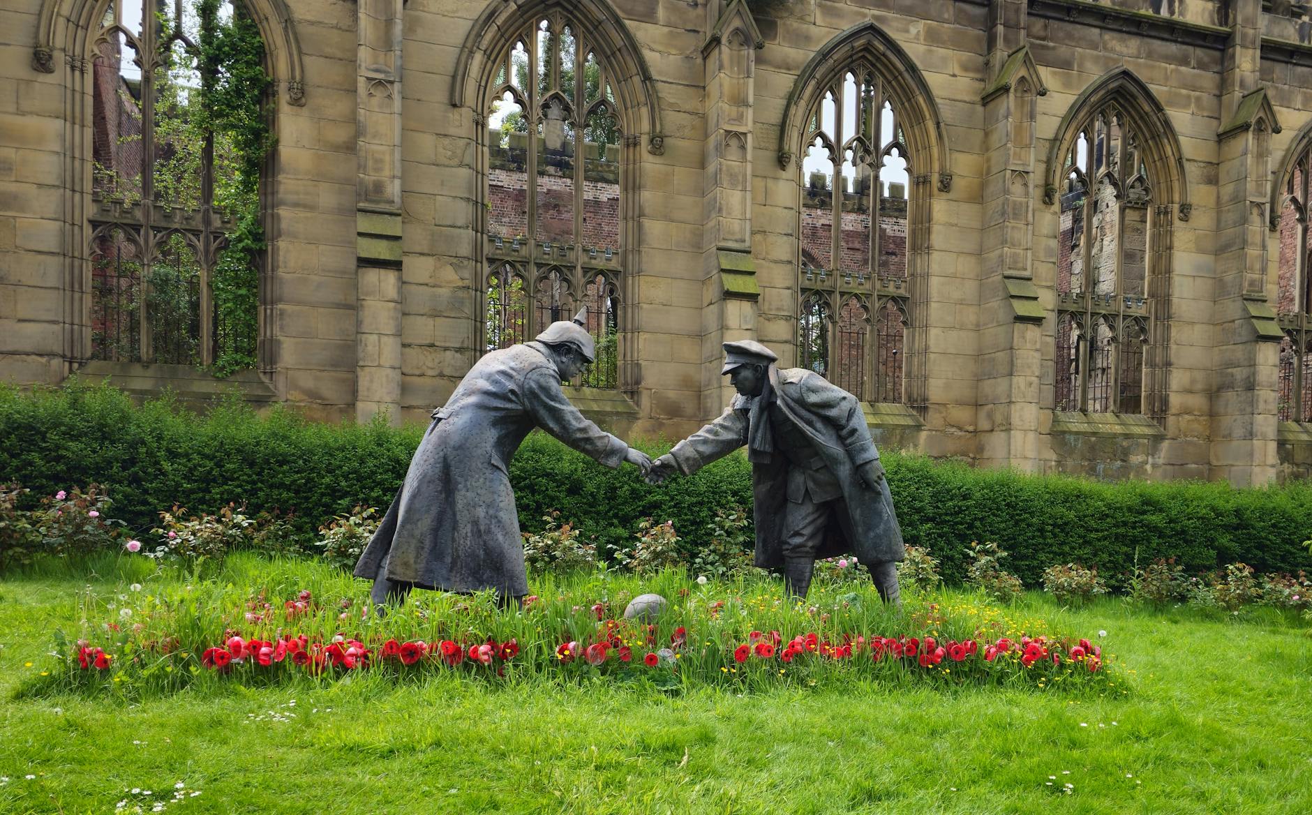 Pomnik żołnierzy podających sobie dłonie w kwitnącym ogrodzie