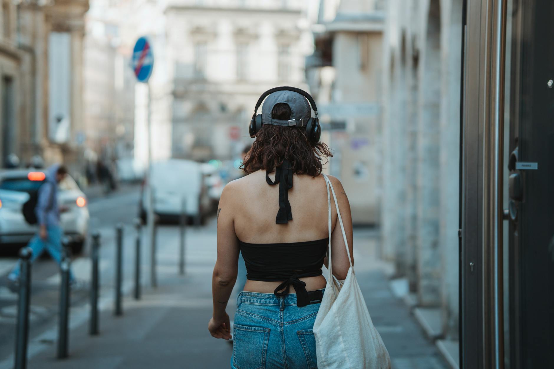 Młoda kobieta w słuchawkach spaceruje ulicą miasta słuchając audio książki