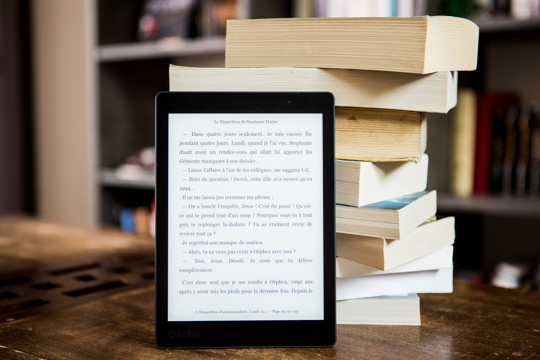 Czytnik ebooków obok stosu papierowych książek na drewnianym stole