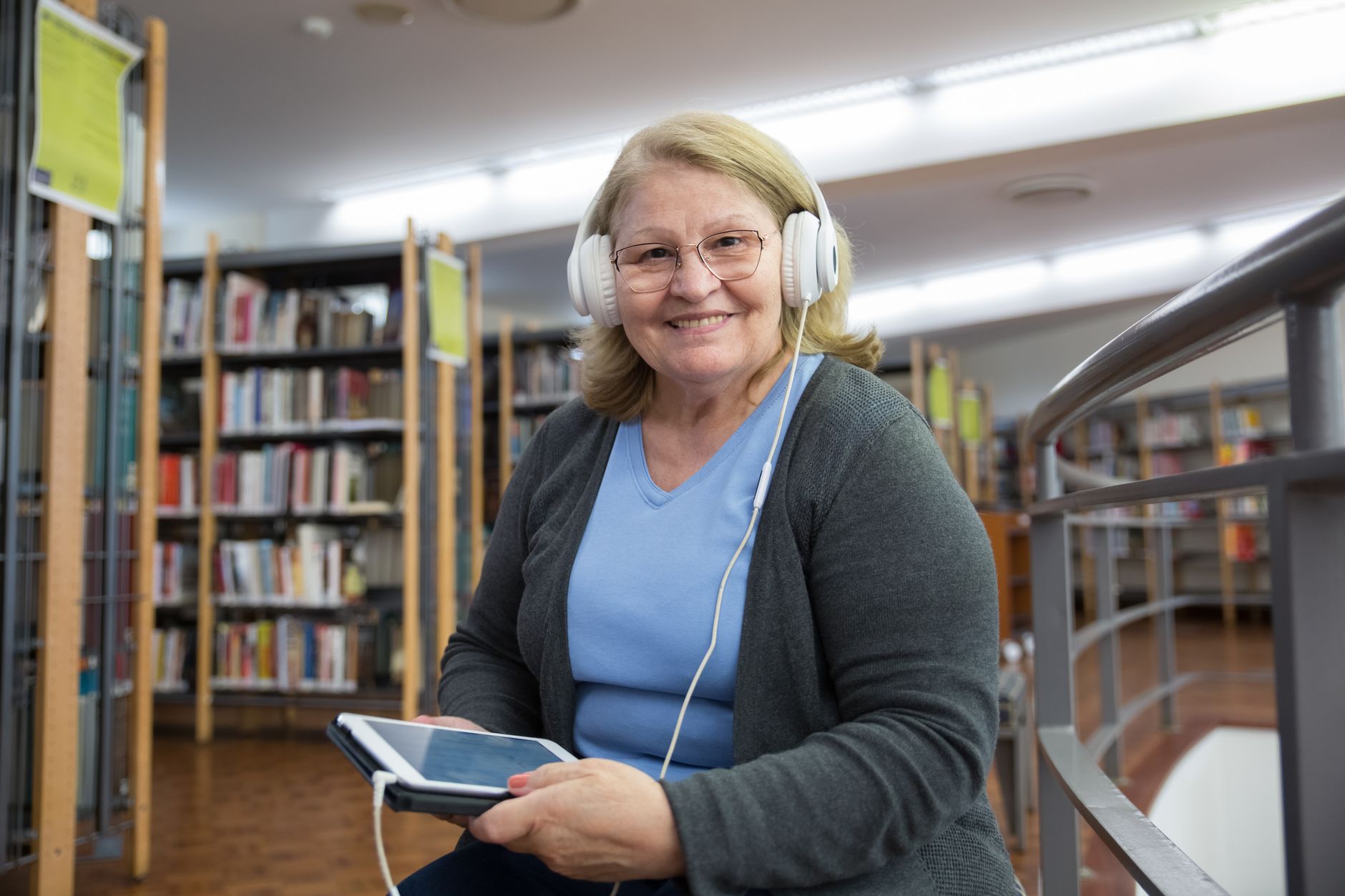 Słuchanie audiobooków w pracy: kiedy pomaga, a kiedy rozprasza i jak to ocenić u siebie Starsza kobieta słucha audiobooka na tablecie w bibliotece